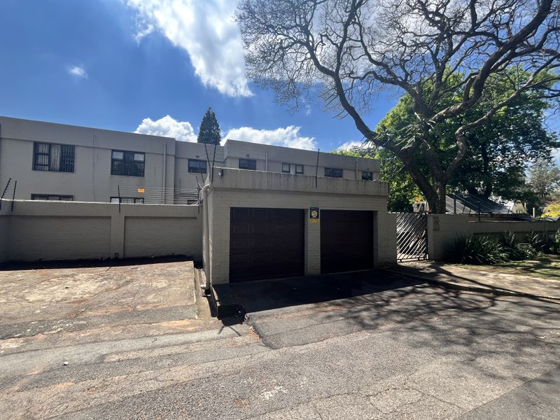 Street-facing view of the property featuring a double garage, boundary wall with electric fencing, and a paved driveway entrance.