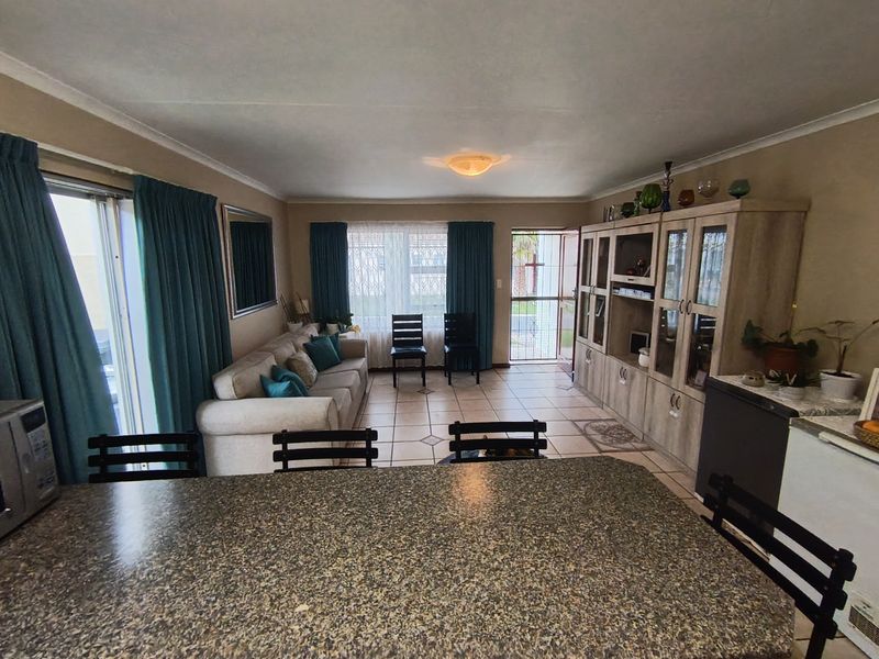 Open-plan living and kitchen area featuring tiled flooring, built-in cabinetry, granite countertops, and direct access to the exterior via a sliding glass door.