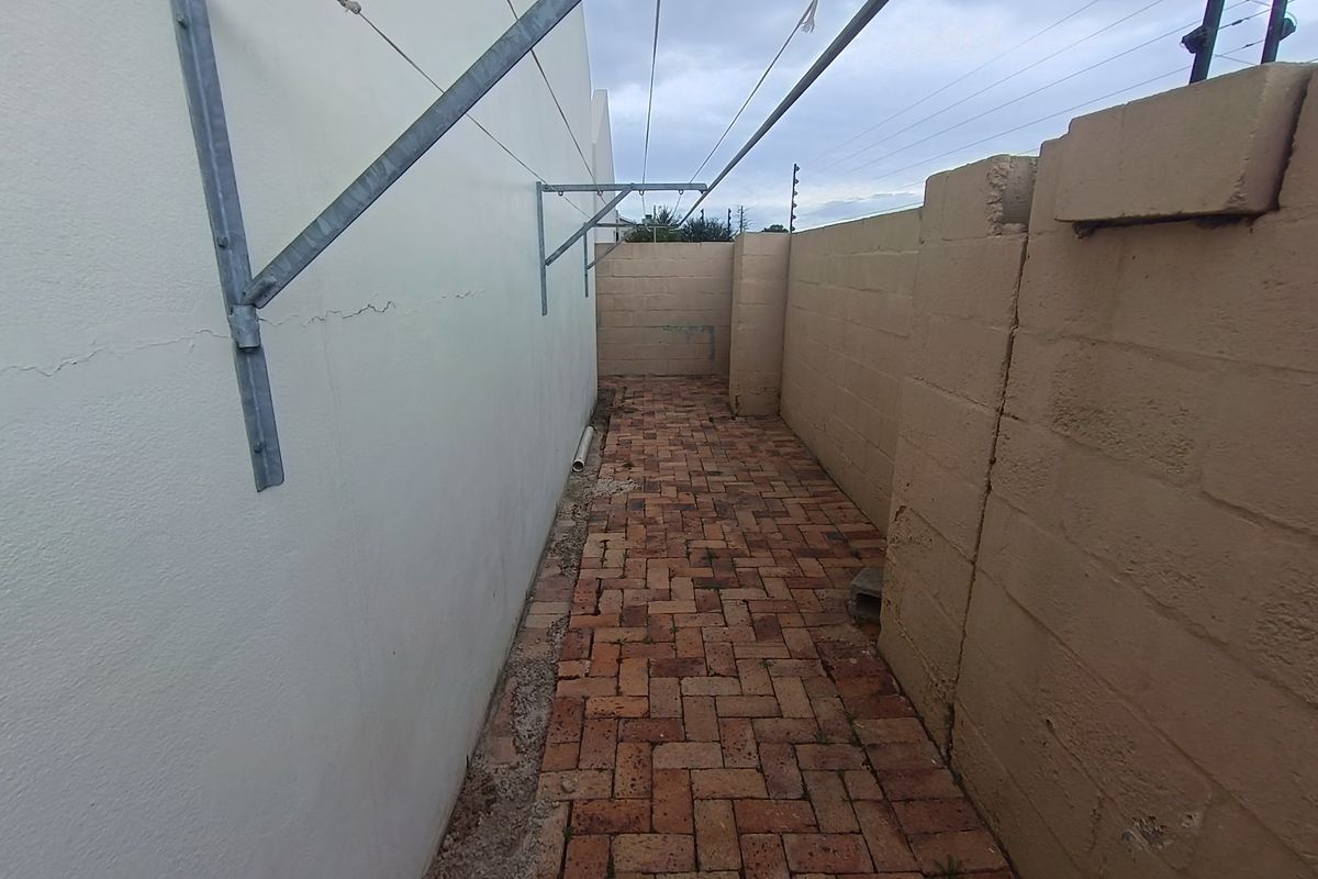 A narrow side courtyard featuring brick paving, a wall-mounted washing line, and perimeter boundary walls with electric fencing.