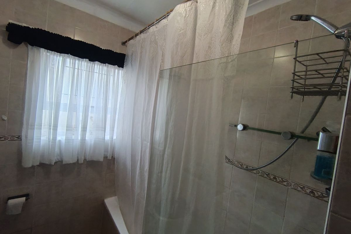 A functional bathroom featuring a bathtub with a shower head, glass screen, and neutral wall tiling.