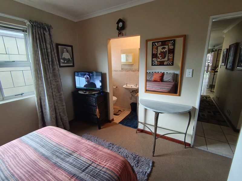 A bedroom featuring carpeted flooring, an en-suite bathroom, and an aluminium window with security bars.