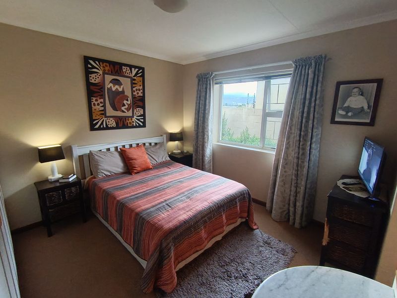 A standard bedroom featuring neutral wall tones, carpeted flooring, and an aluminium-framed window providing natural light.