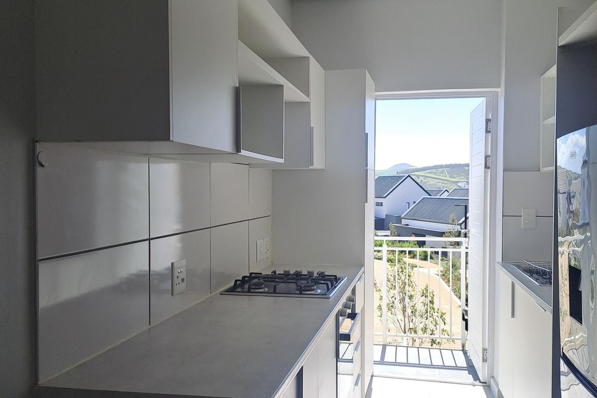 Modern galley-style kitchen featuring white cabinetry, gas hob, built-in oven, and tiled finishes, with direct access to a balcony.