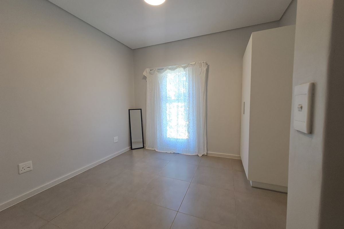 A clean, neutral-toned bedroom featuring tiled flooring, a built-in wardrobe, and ample natural light, providing a versatile space ready for personalization.