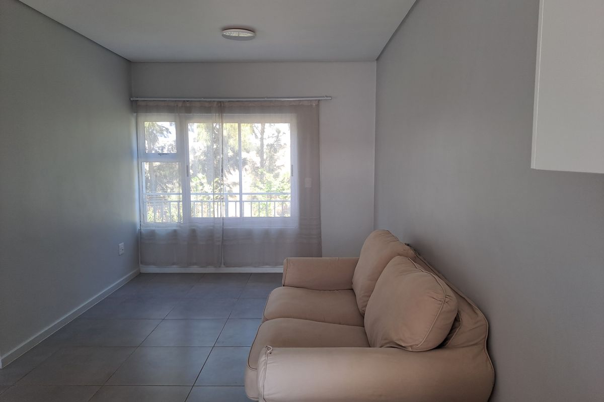 A bright living room featuring neutral grey walls, large sliding windows, and modern tiled flooring, offering a clean and versatile space.