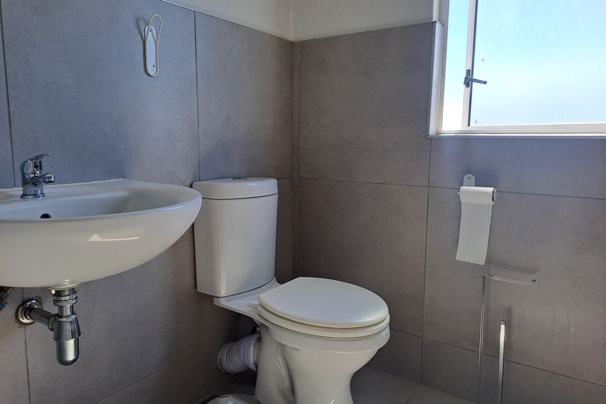 A clean and modern bathroom featuring grey wall tiles, a white pedestal basin, and a standard toilet with a window for natural light.