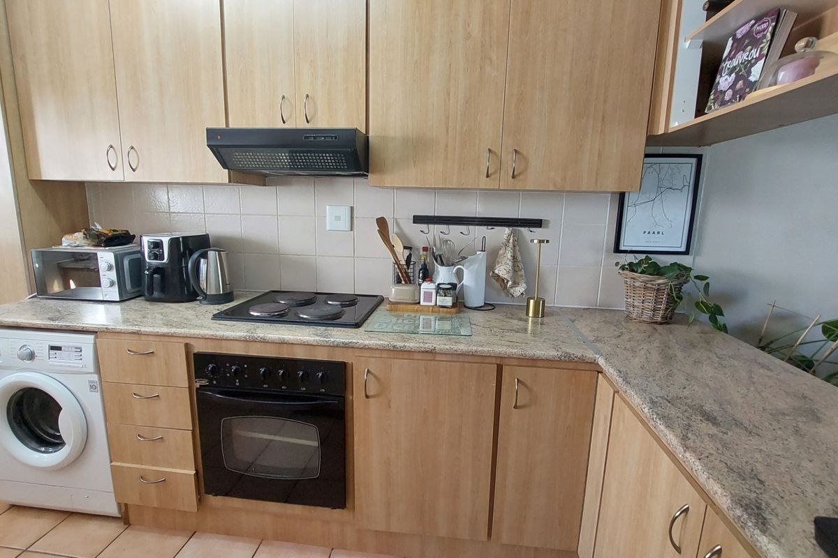 Functional kitchen featuring light wood cabinetry, granite countertops, built-in oven, electric hob, extractor fan, and an integrated washing machine.