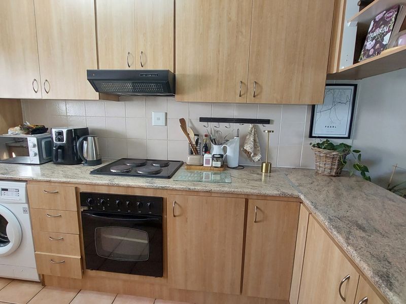 Functional kitchen featuring light wood cabinetry, granite countertops, built-in oven, electric hob, extractor fan, and an integrated washing machine.
