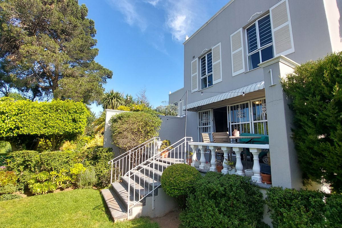 Rear view of the townhouse featuring a raised patio with balustrade, external staircase, and established garden surroundings.