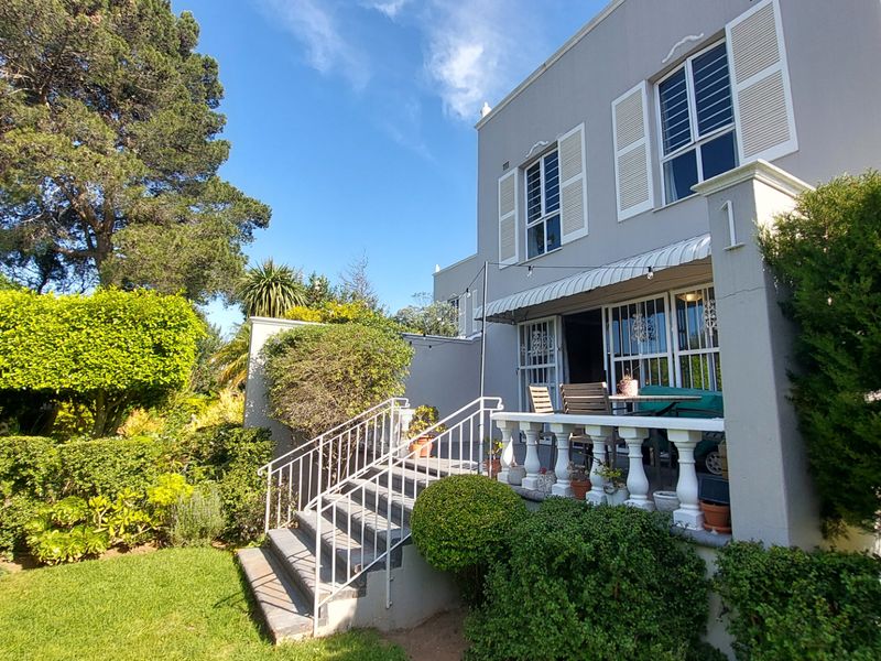 Rear view of the townhouse featuring a raised patio with balustrade, external staircase, and established garden surroundings.