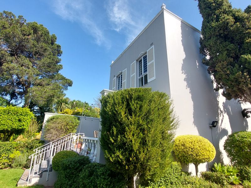 Rear elevation of the townhouse featuring a staircase with balustrade, white window shutters, and well-maintained surrounding garden landscaping.