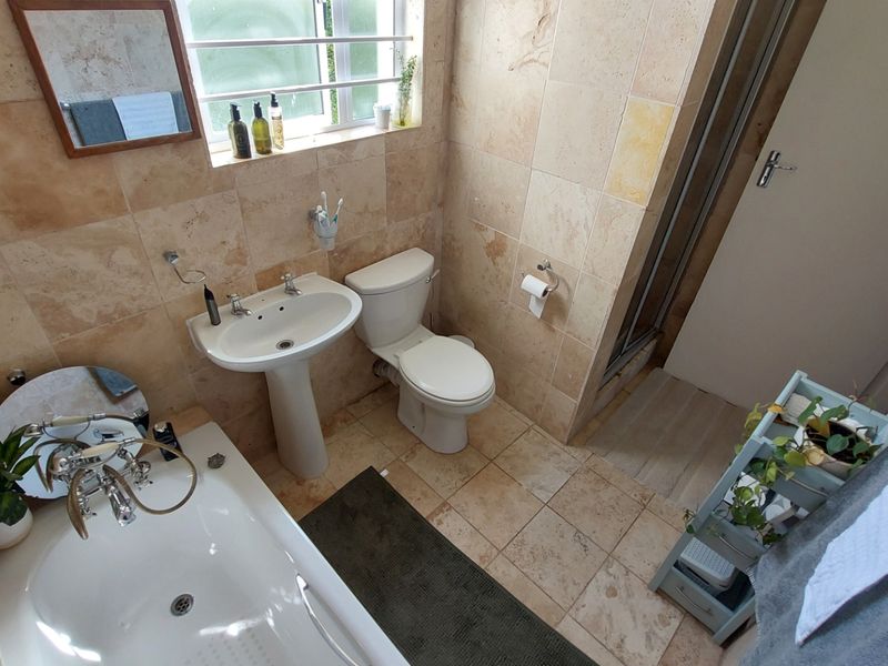A well-maintained bathroom featuring travertine wall and floor tiles, a pedestal basin, a toilet, a bathtub, and a separate shower enclosure.