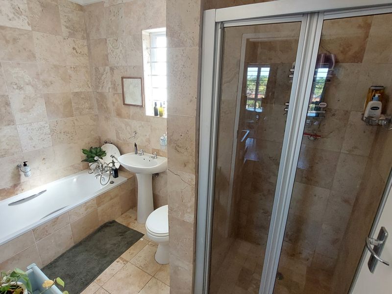 A well-maintained bathroom featuring floor-to-ceiling travertine tiling, a pedestal basin, a built-in bathtub, and a separate glass-enclosed shower.
