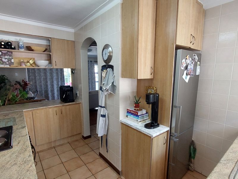 A functional kitchen featuring laminate cabinetry, granite countertops, and ceramic tiling, offering a practical layout with an archway leading to the living area.
