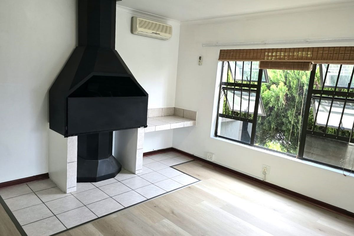 A bright, empty living area featuring a prominent built-in fireplace with a tiled hearth, laminate flooring, and a wall-mounted air conditioning unit.