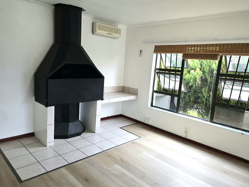A bright, empty living area featuring a prominent built-in fireplace with a tiled hearth, laminate flooring, and a wall-mounted air conditioning unit.