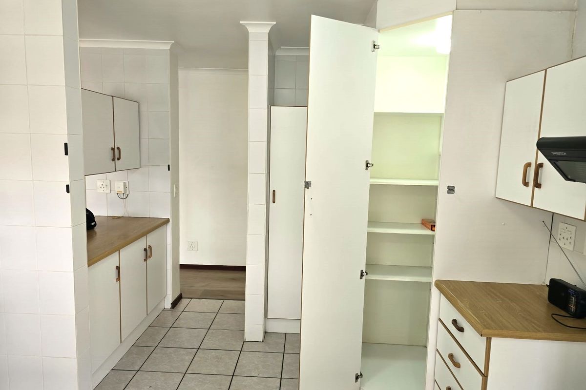 A functional kitchen area featuring white built-in cabinetry, laminate countertops, tiled flooring, and a dedicated pantry cupboard.