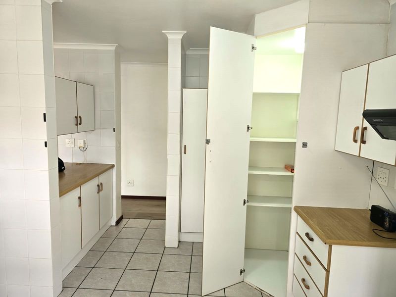 A functional kitchen area featuring white built-in cabinetry, laminate countertops, tiled flooring, and a dedicated pantry cupboard.