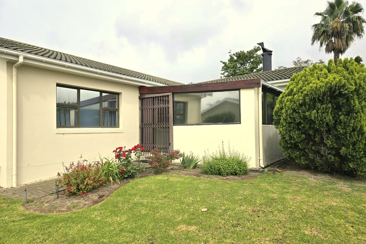 Rear view of the property featuring a tiled roof, aluminium window frames, and a secure entrance gate, set against a well-maintained garden.