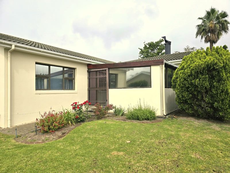 Rear view of the property featuring a tiled roof, aluminium window frames, and a secure entrance gate, set against a well-maintained garden.