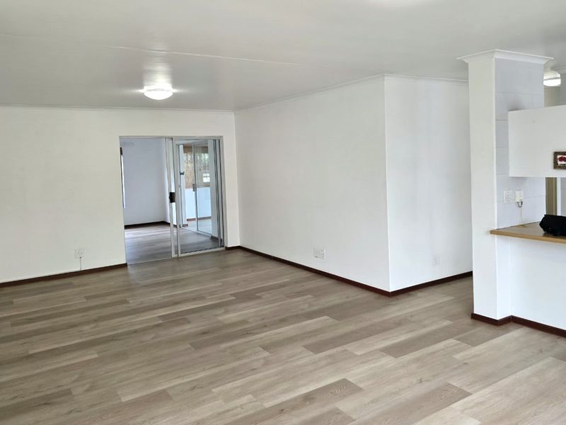 Spacious open-plan living area featuring modern laminate flooring, a breakfast bar, and a sliding glass door leading to an adjacent room.