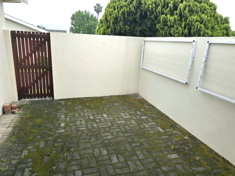 A private rear courtyard featuring paved flooring with moss growth, a secure timber gate, and wall-mounted clotheslines against a boundary wall.