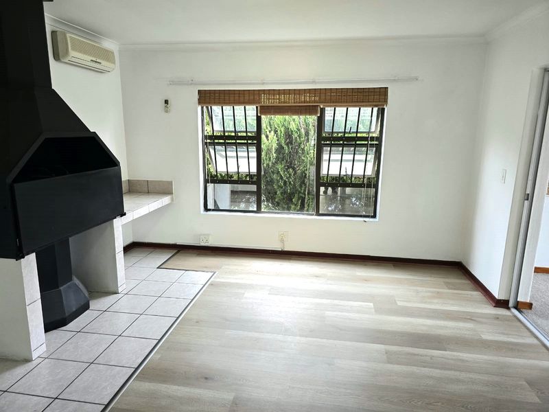 Bright living area featuring a built-in fireplace with tiled hearth, laminate flooring, and a wall-mounted air conditioning unit.