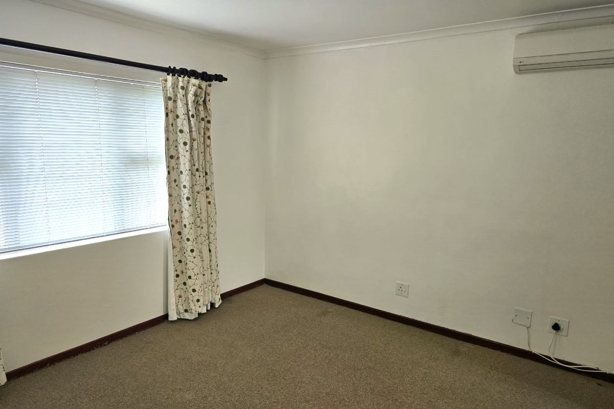 A clean, empty bedroom featuring neutral walls, carpeted flooring, and a wall-mounted air conditioning unit.