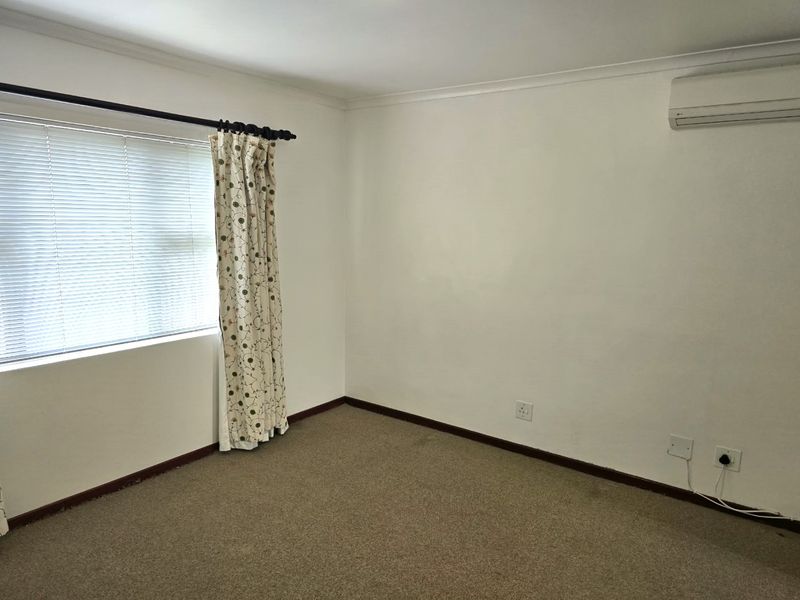 A clean, empty bedroom featuring neutral walls, carpeted flooring, and a wall-mounted air conditioning unit.