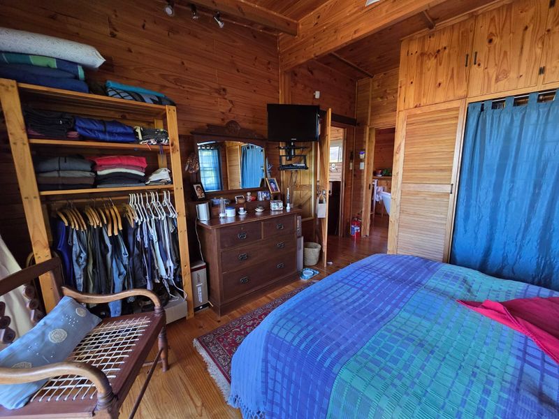 A bedroom featuring timber wall cladding, wooden flooring, and built-in cupboards, offering a rustic aesthetic.