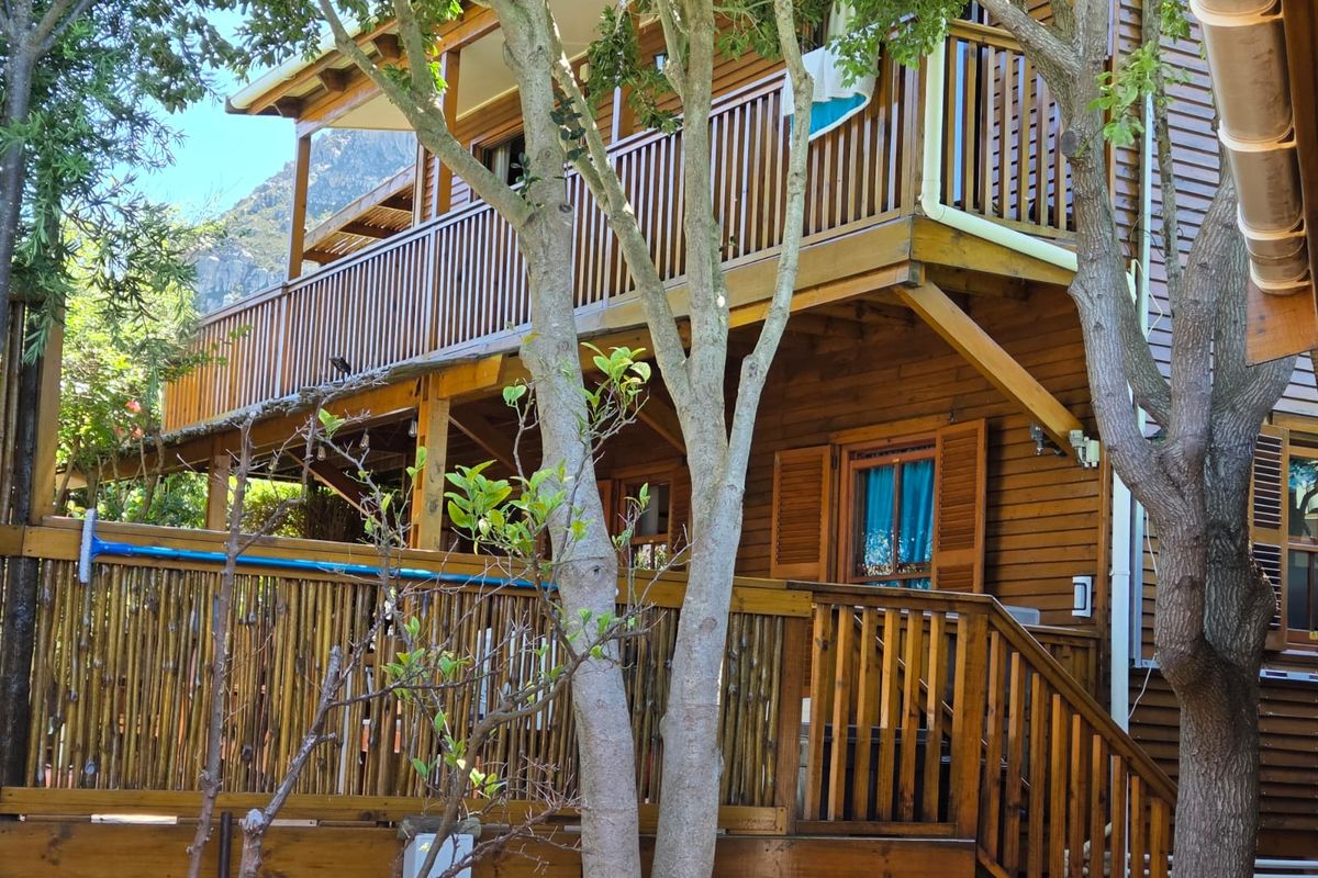 A rear view of a timber-clad house featuring multi-level wooden decking, balustrades, and traditional timber shutters set against a natural landscape.