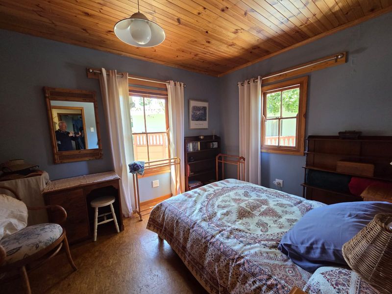 A cozy bedroom featuring a warm timber tongue and groove ceiling, cork flooring, and dual windows with timber frames.