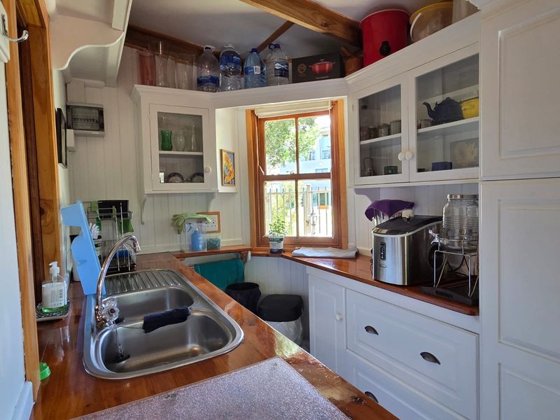 A compact kitchen featuring wooden countertops, double bowl stainless steel sink, and white built-in cabinetry with glass-fronted wall units.