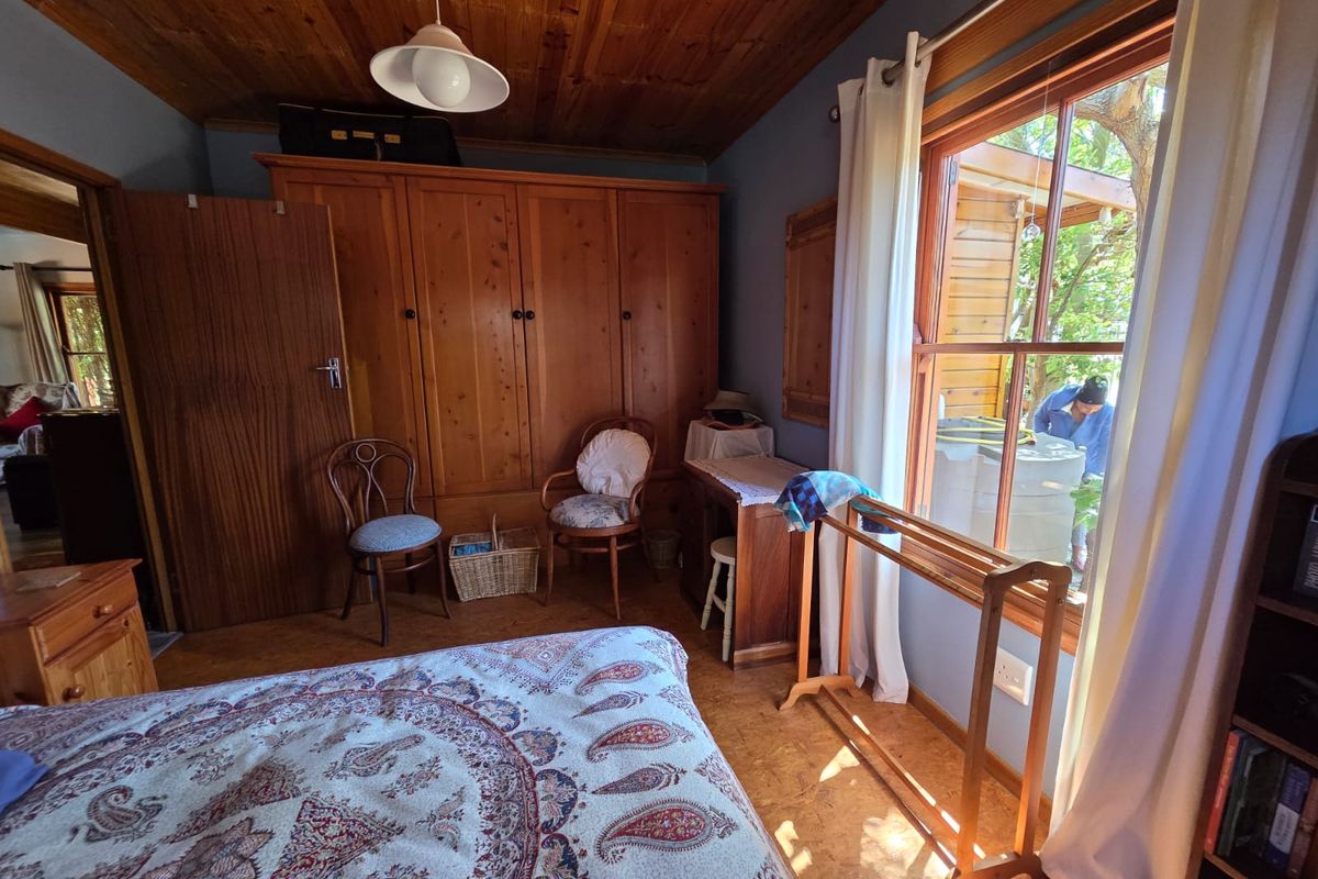A cozy bedroom featuring a timber ceiling, cork flooring, and a large built-in wooden wardrobe, with natural light entering through a sash window.