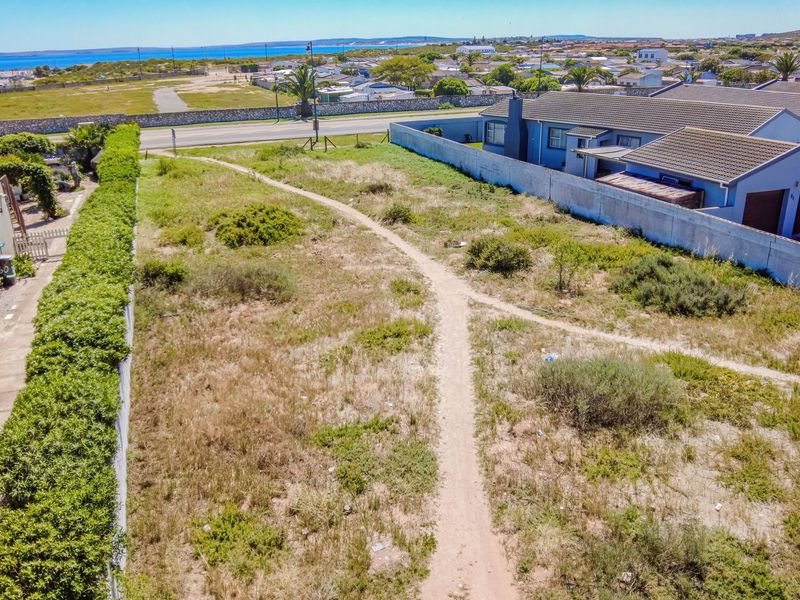 An aerial view of a vacant residential plot featuring established boundary walls and surrounding neighborhood infrastructure with distant coastal views.