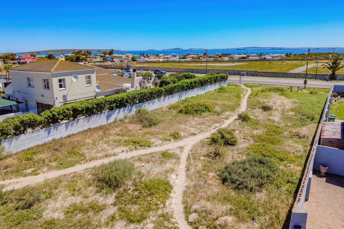 Aerial view of a vacant residential plot featuring boundary walls, established hedging, and a paved driveway, situated in a coastal neighborhood.