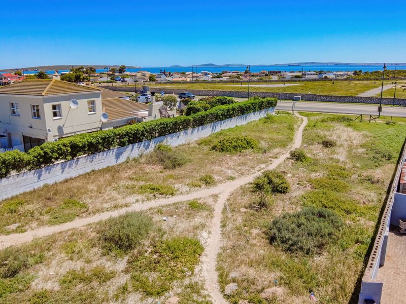 Aerial view of a vacant residential plot featuring boundary walls, established hedging, and a paved driveway, situated in a coastal neighborhood.