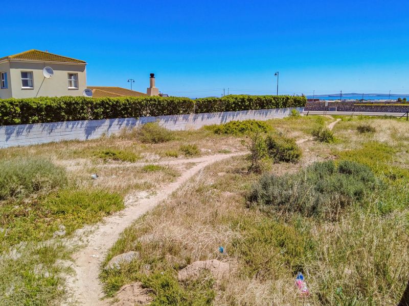 A vacant residential plot featuring a boundary wall and established hedging, offering a clear view of the surrounding neighborhood and distant landscape.