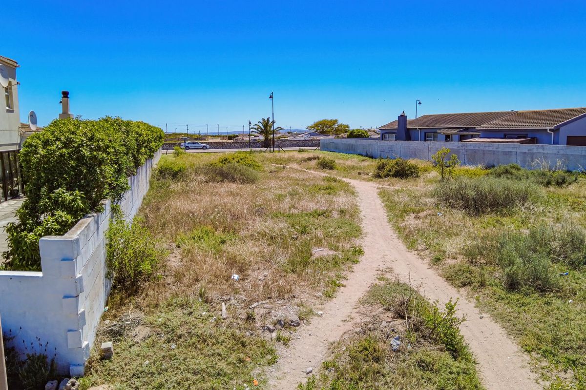 A view of a vacant residential plot featuring a boundary wall, paved patio area, and natural vegetation.