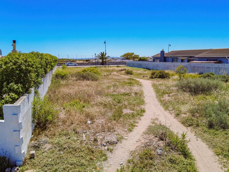 A view of a vacant residential plot featuring a boundary wall, paved patio area, and natural vegetation.