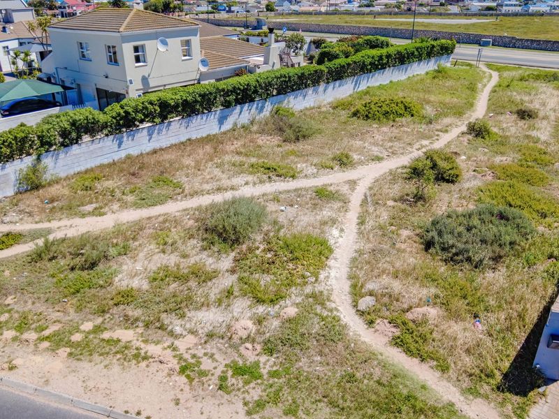 An aerial view of a vacant residential plot featuring natural vegetation, boundary walls, and direct street access in a developed neighborhood.