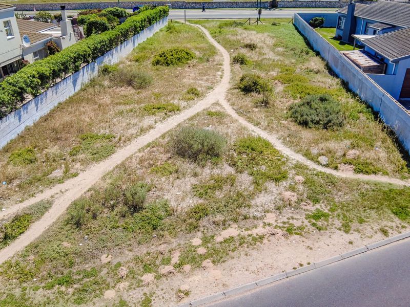 Aerial view of a vacant residential plot featuring boundary walls and access to a paved road, offering potential for future development.