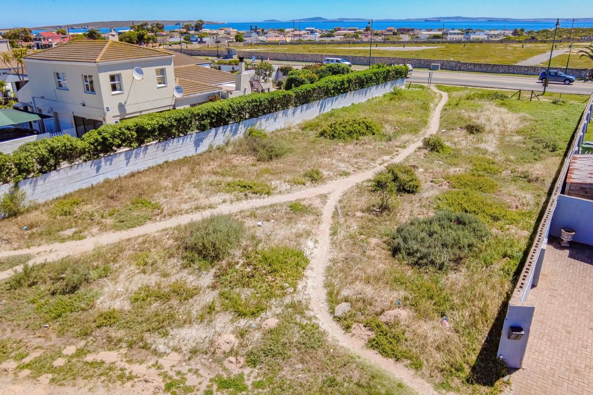 Aerial view of a vacant residential plot featuring boundary walls, established hedges, and a paved driveway section, situated in a coastal neighborhood.