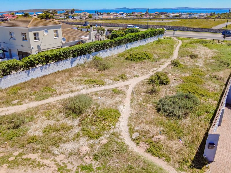 Aerial view of a vacant residential plot featuring boundary walls, established hedges, and a paved driveway section, situated in a coastal neighborhood.