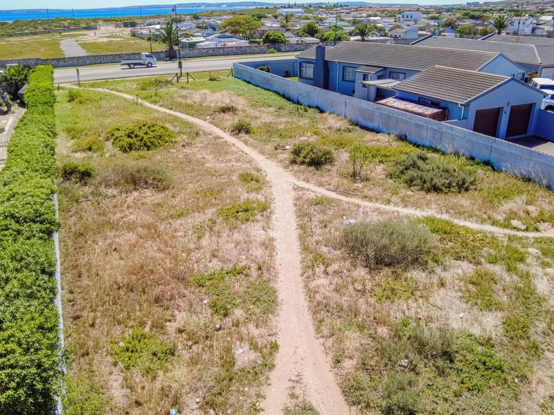 An aerial view of a vacant residential plot featuring natural vegetation, boundary walls, and proximity to local infrastructure and coastal surroundings.