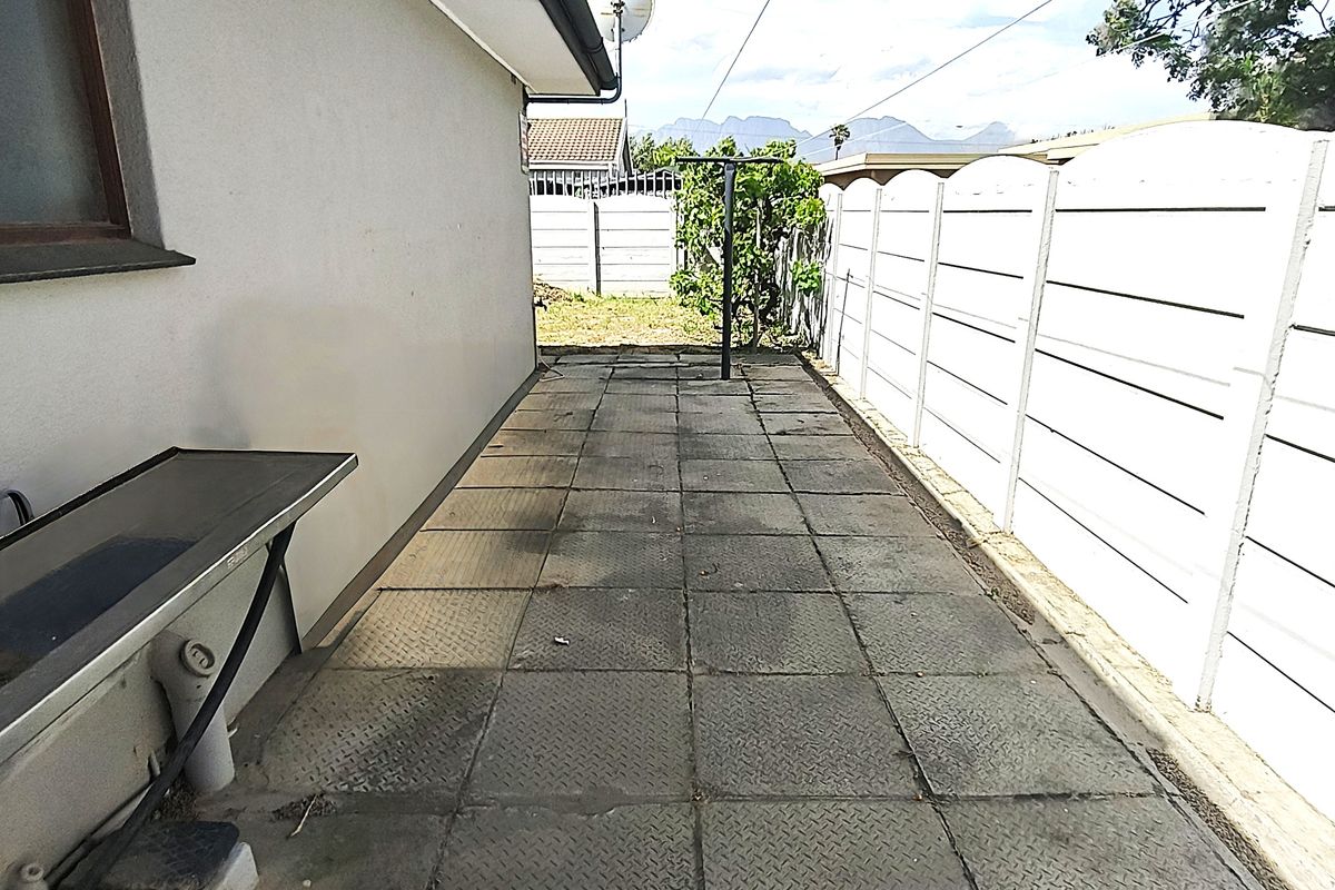 A side exterior walkway featuring paved flooring and a precast concrete boundary wall, providing access along the side of the house.