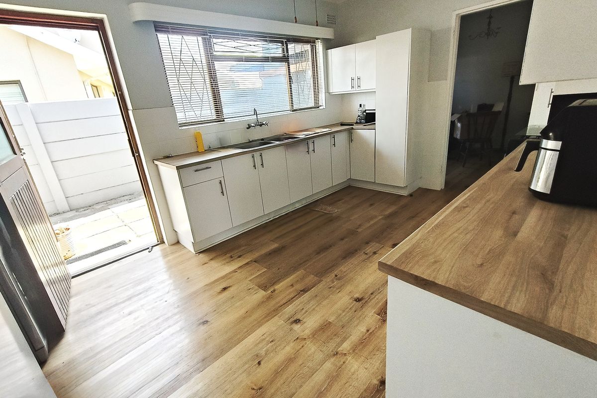 A clean, modern kitchen featuring white cabinetry, wood-look laminate countertops, and durable flooring, with direct access to an outdoor area.