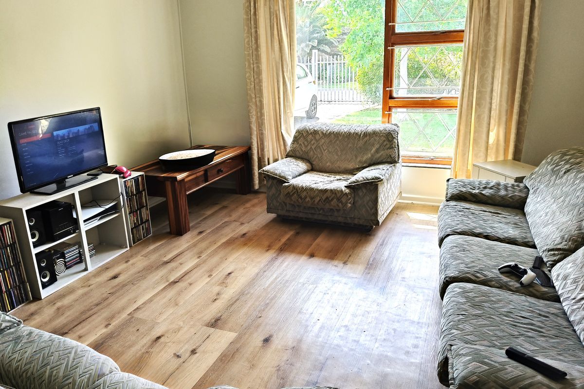 A comfortable living room featuring modern laminate flooring and a large window that provides natural light and views of the front garden.