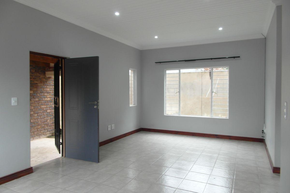 A bright, empty living room featuring neutral grey walls, tiled flooring, timber skirting, and recessed downlights, offering a clean canvas for personalization.