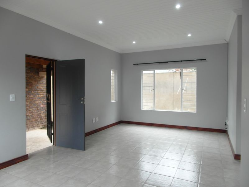A bright, empty living room featuring neutral grey walls, tiled flooring, timber skirting, and recessed downlights, offering a clean canvas for personalization.